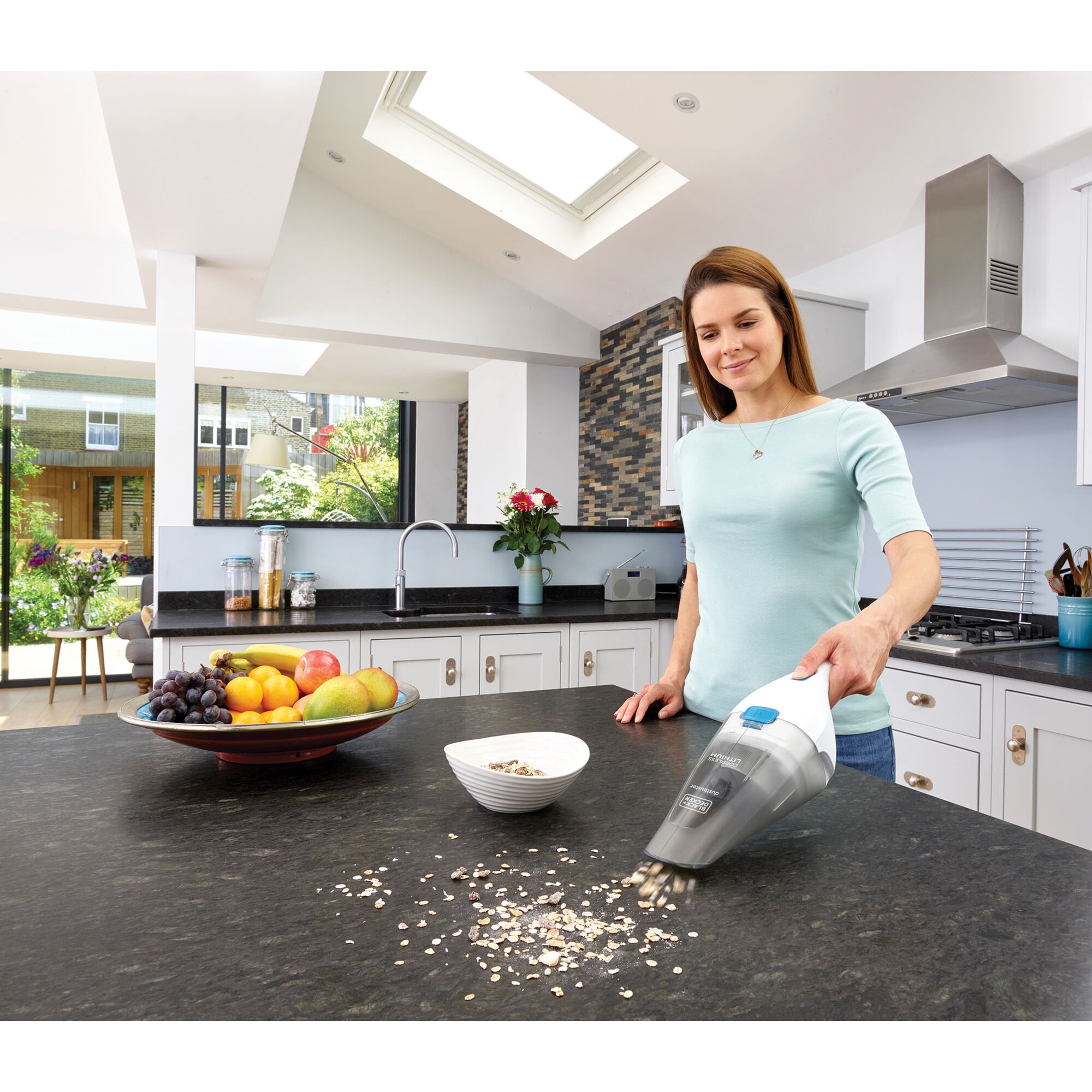 BLACKDECKER NVC115JLW handheld vacuum cleaning kitchen countertop with scattered oats near a fruit bowl.