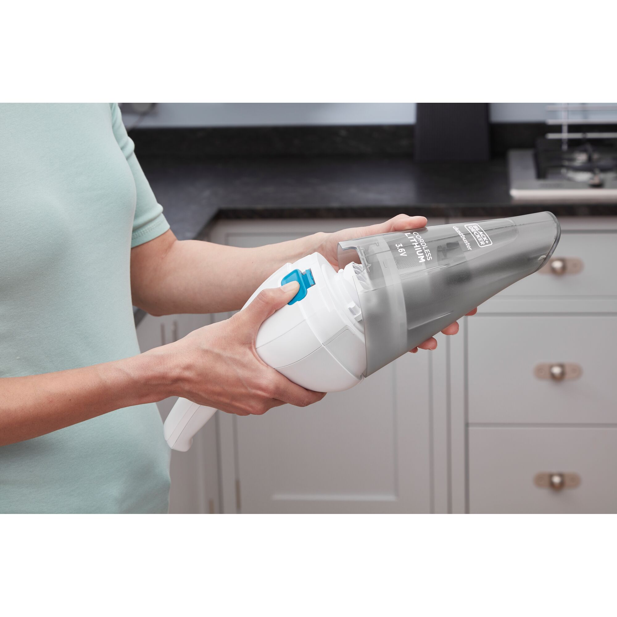 A person is holding and cleaning a BLACK+DECKER handheld vacuum cleaner in a kitchen.