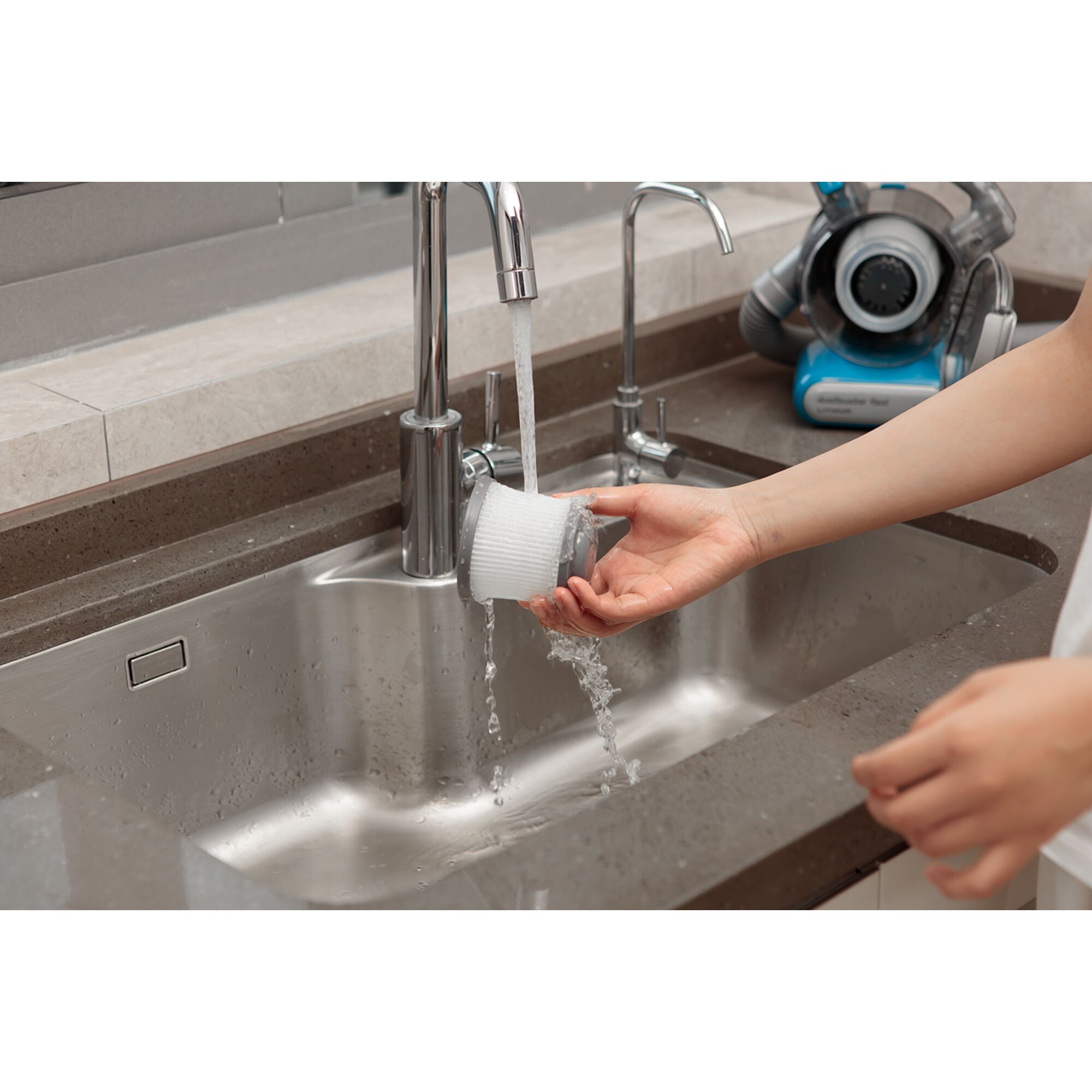 BLACKDECKER PDB315JB vacuum filter being rinsed under faucet in kitchen sink, vacuum unit in background.