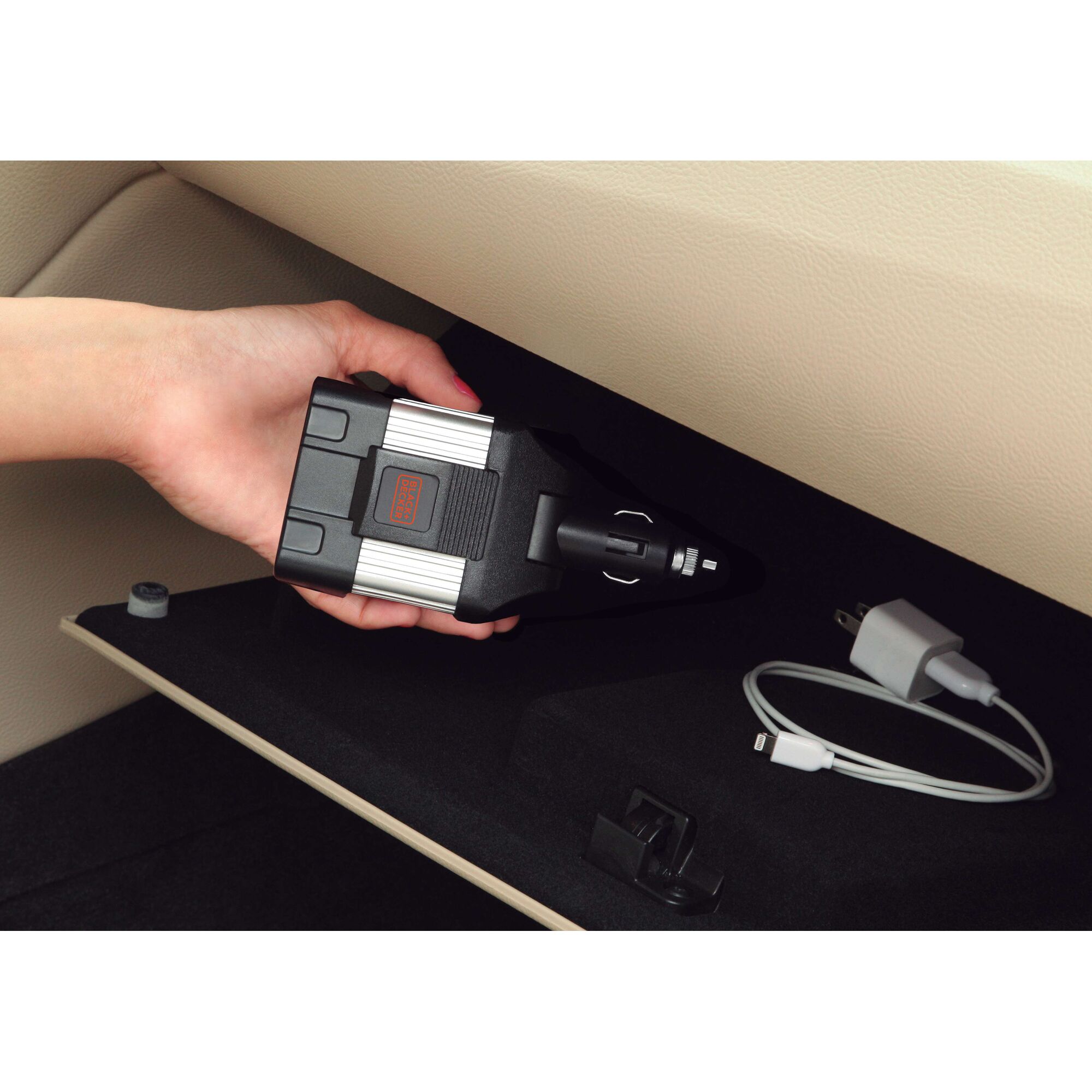 BLACKDECKER PI100LA power inverter held in hand inside car glove compartment, charger and cable nearby.
