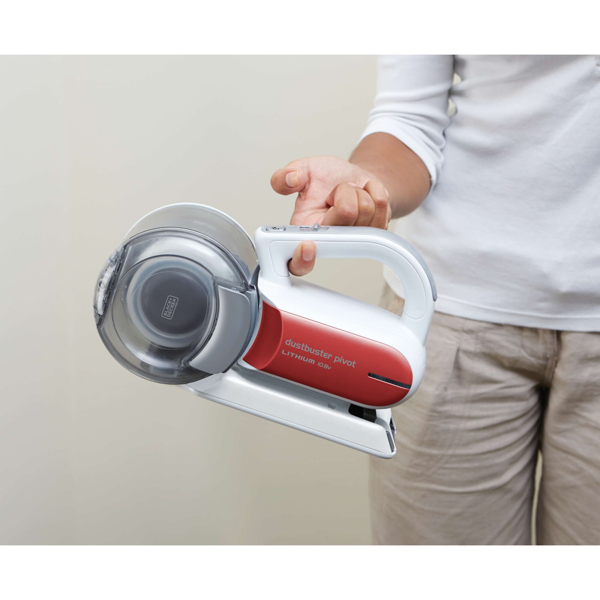 A person holding a BLACK+DECKER Dustbuster Pivot Lithium 10.8V handheld vacuum cleaner with a red and white body.