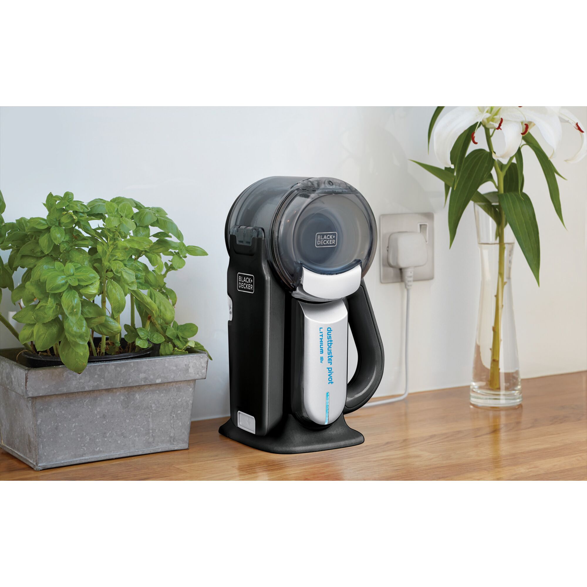 BLACKDECKER PV1820BK handheld vacuum in docking station on wooden countertop next to potted plant and vase.