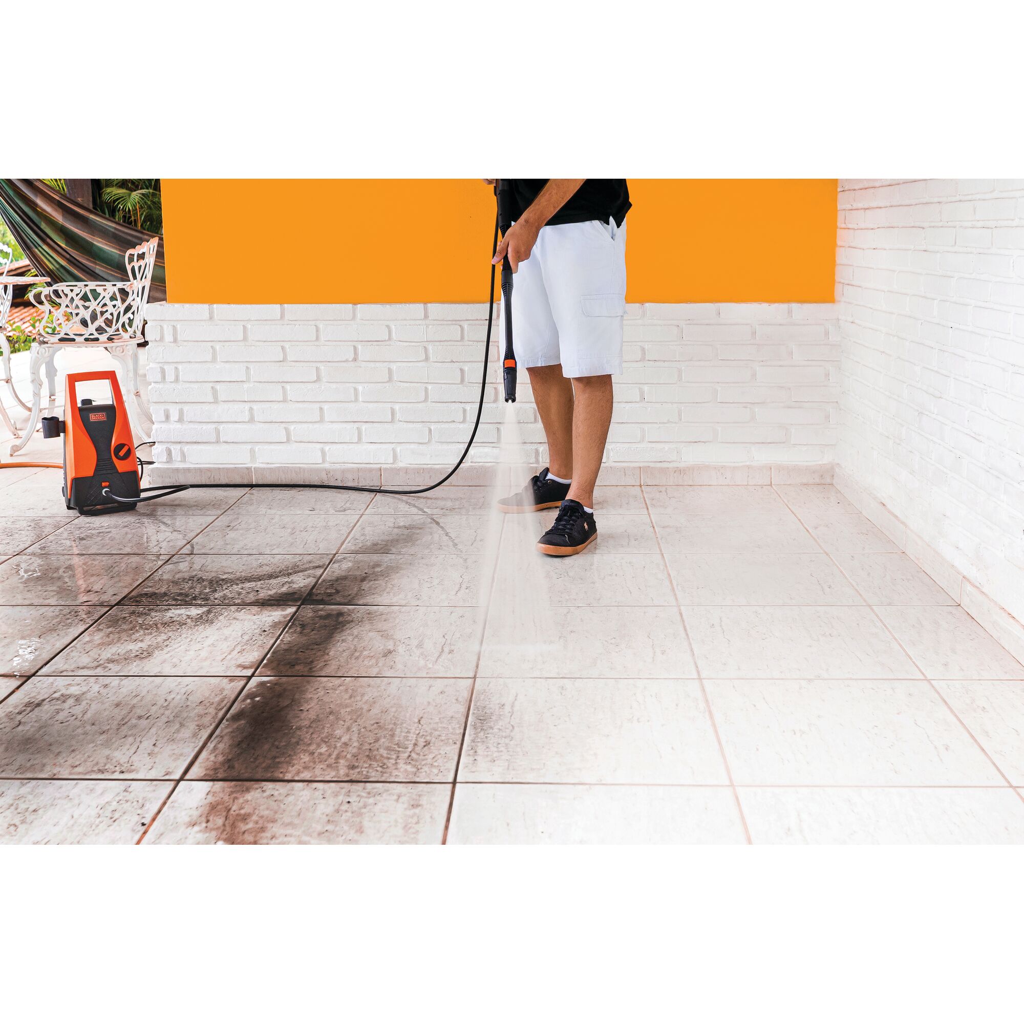 BLACKDECKER PW1450TD pressure washer cleaning dirty tiles, side view of orange and white unit in use.