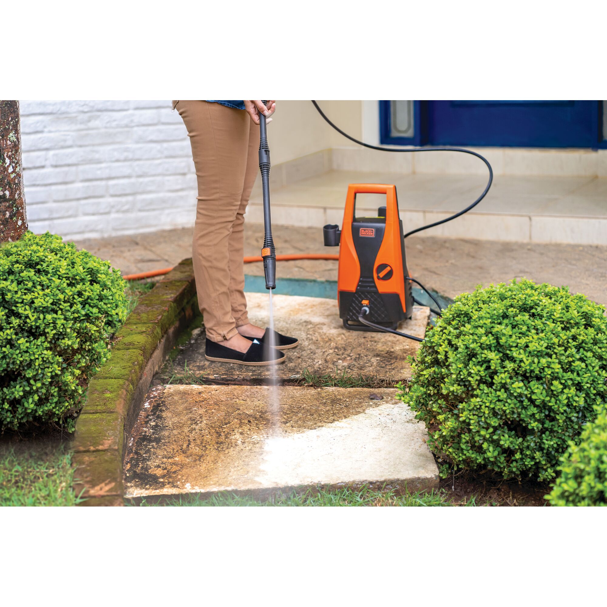BLACKDECKER PW1450TD pressure washer cleaning outdoor stone path, orange and black unit shown.