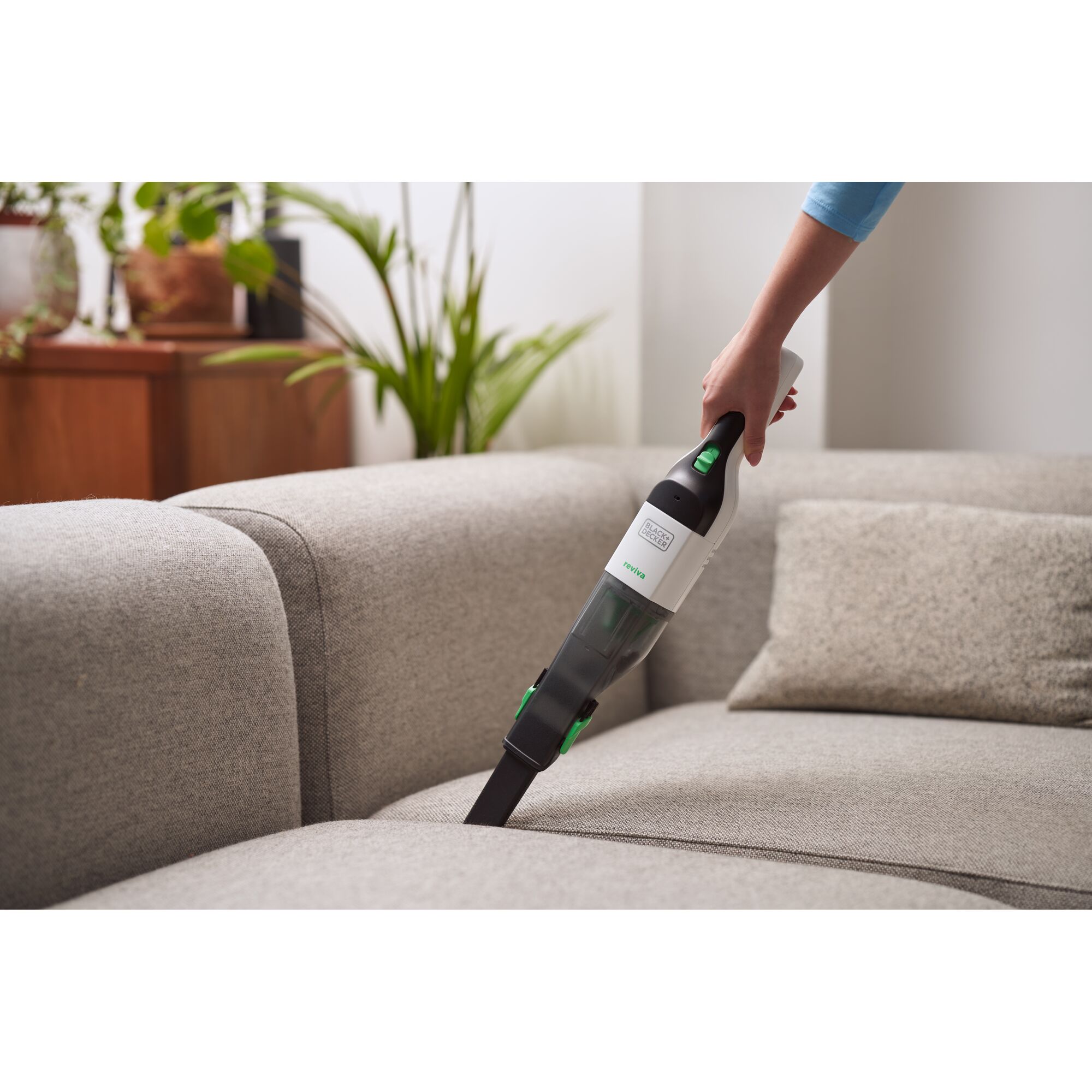 BLACKDECKER REVHV8C handheld vacuum cleaner in use on a gray sofa in a living room setting.