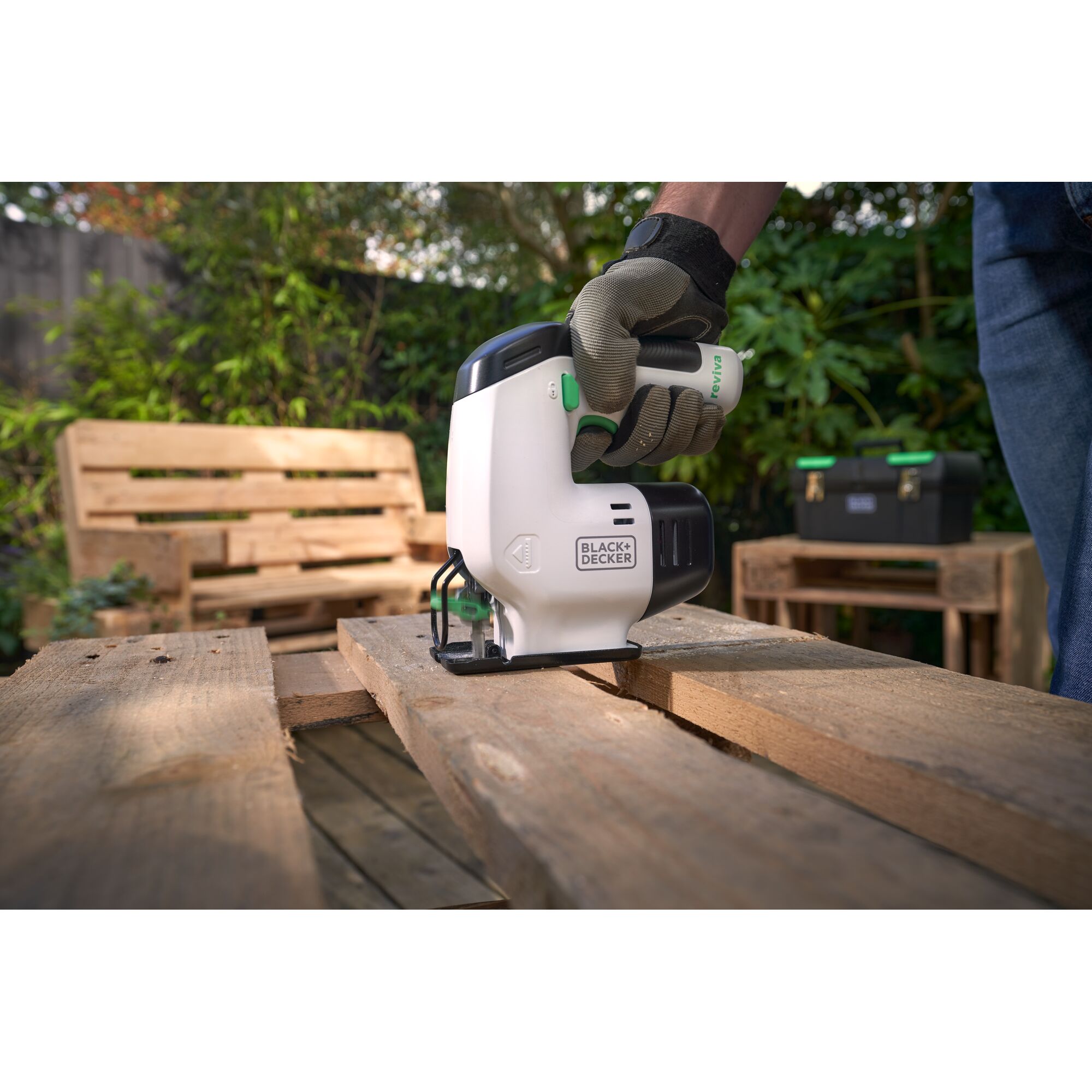 BLACKDECKER REVJ12C jigsaw cutting wood outdoors, gloved hand holding tool, outdoor furniture in background.