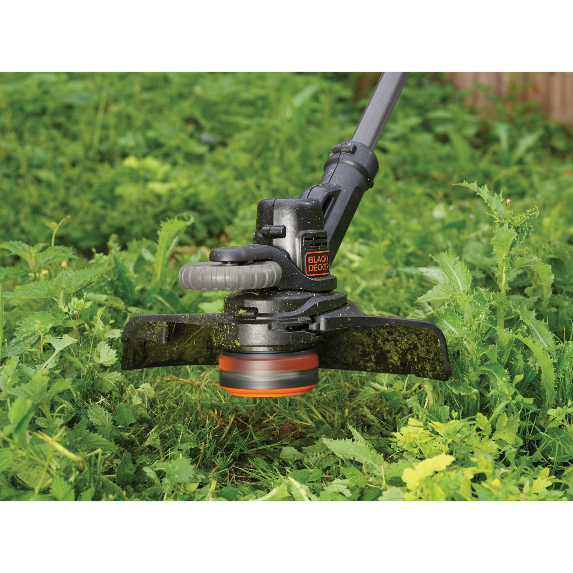 BLACKDECKER STC1820EPCF grass trimmer in use cutting green weeds outdoors.