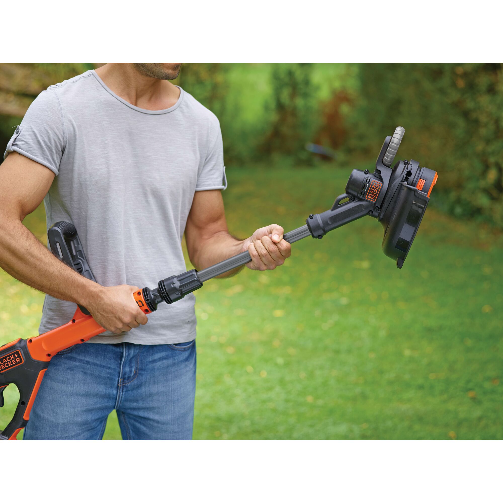 BLACKDECKER STC1820EPC grass trimmer held outdoors, orange and black cordless design, close-up view.