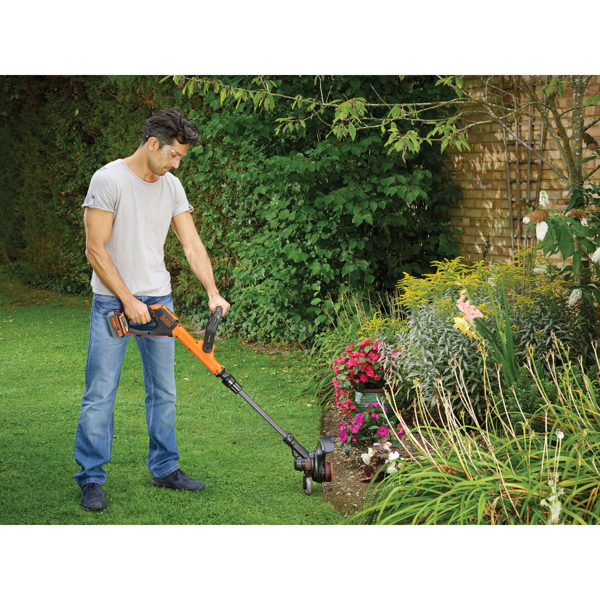 BLACKDECKER STC1840EPC grass trimmer used to edge lawn beside flowerbed outdoors.
