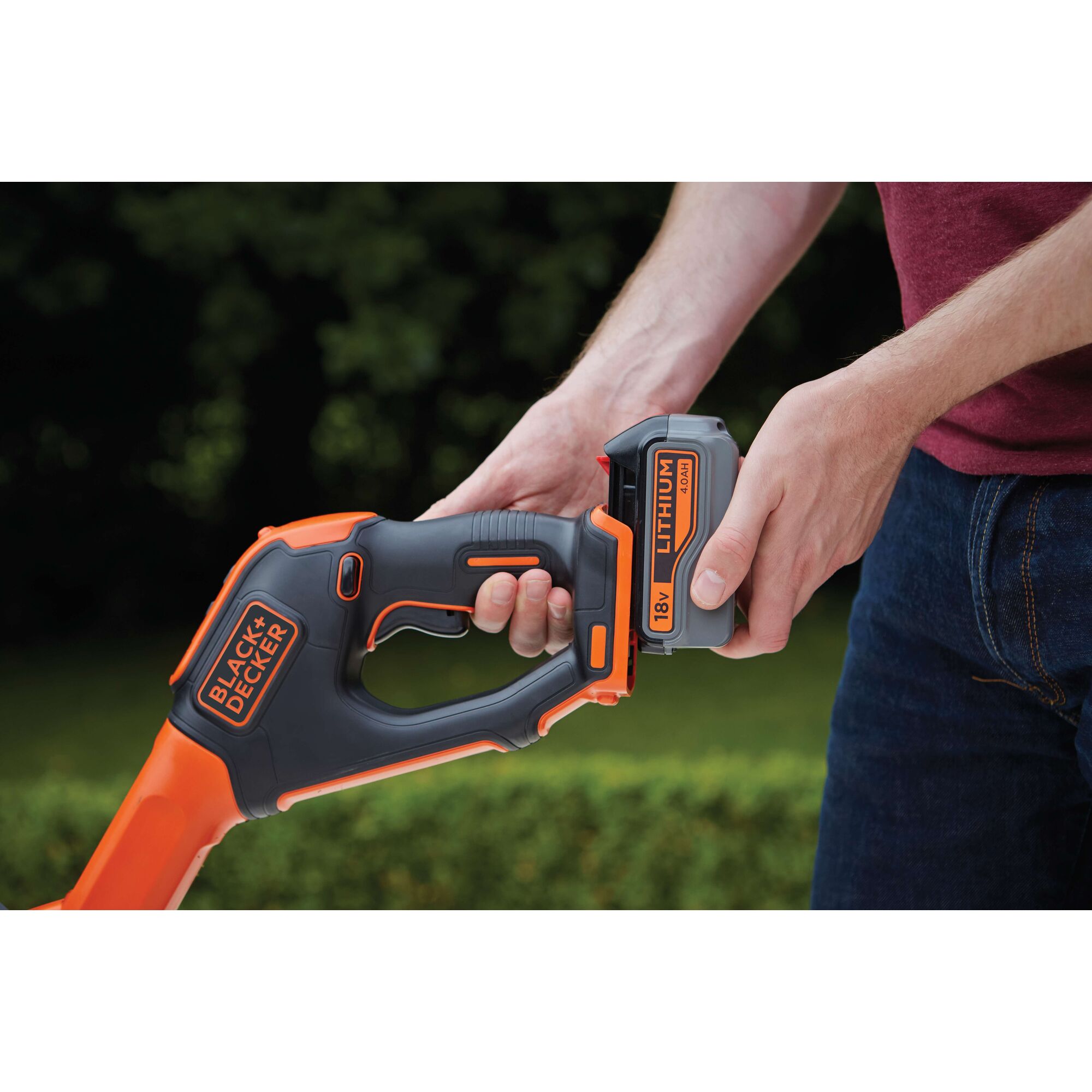 Photo of BLACKDECKER STC1840EPC trimmer handle with 18V lithium battery being inserted outdoors.
