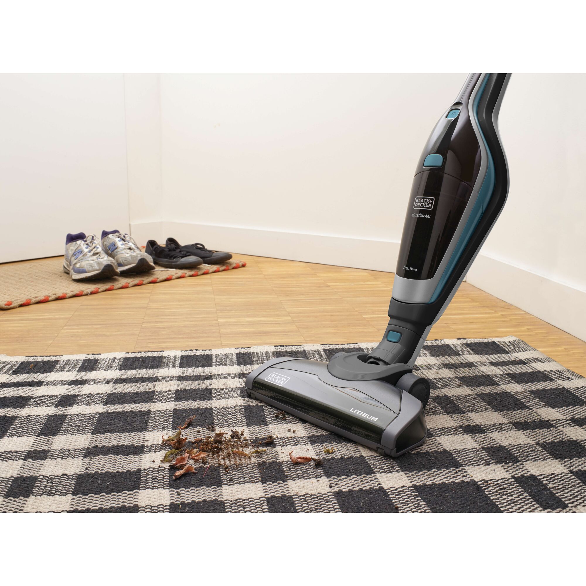 BLACKDECKER SVA420B stick vacuum cleaning debris from checkered rug, side angle, shoes in background.