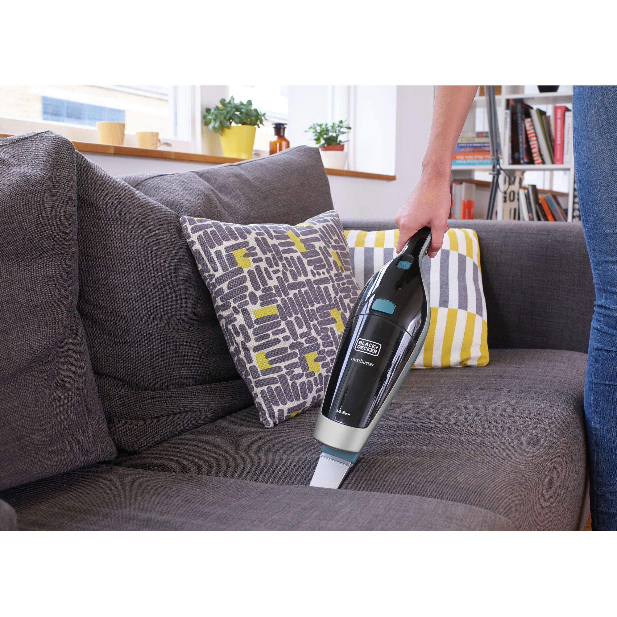 BLACKDECKER SVA420B handheld vacuum cleaning a gray sofa in a living room.