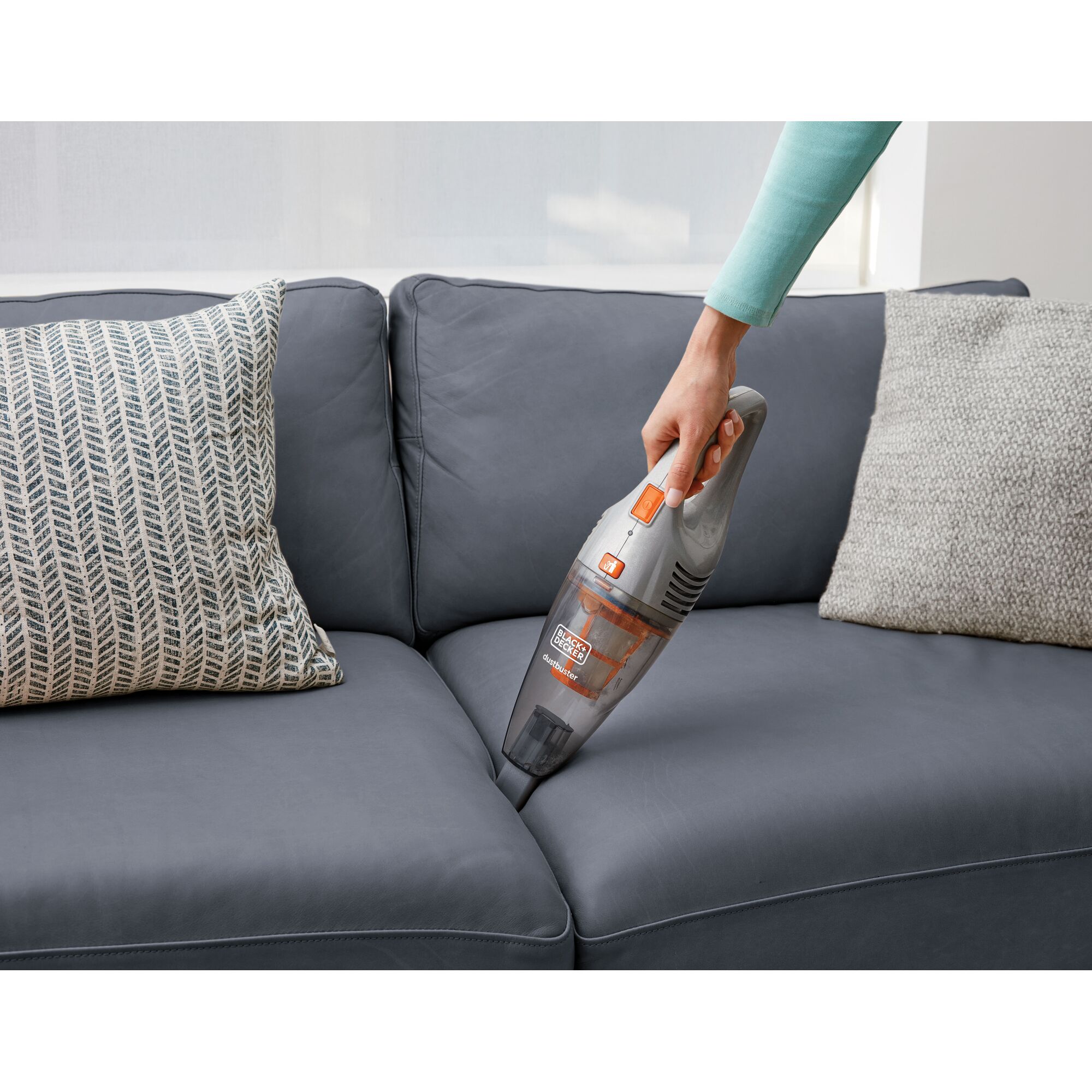 BLACKDECKER SVB420J handheld vacuum cleaning sofa corner with grey cushions and patterned pillow.