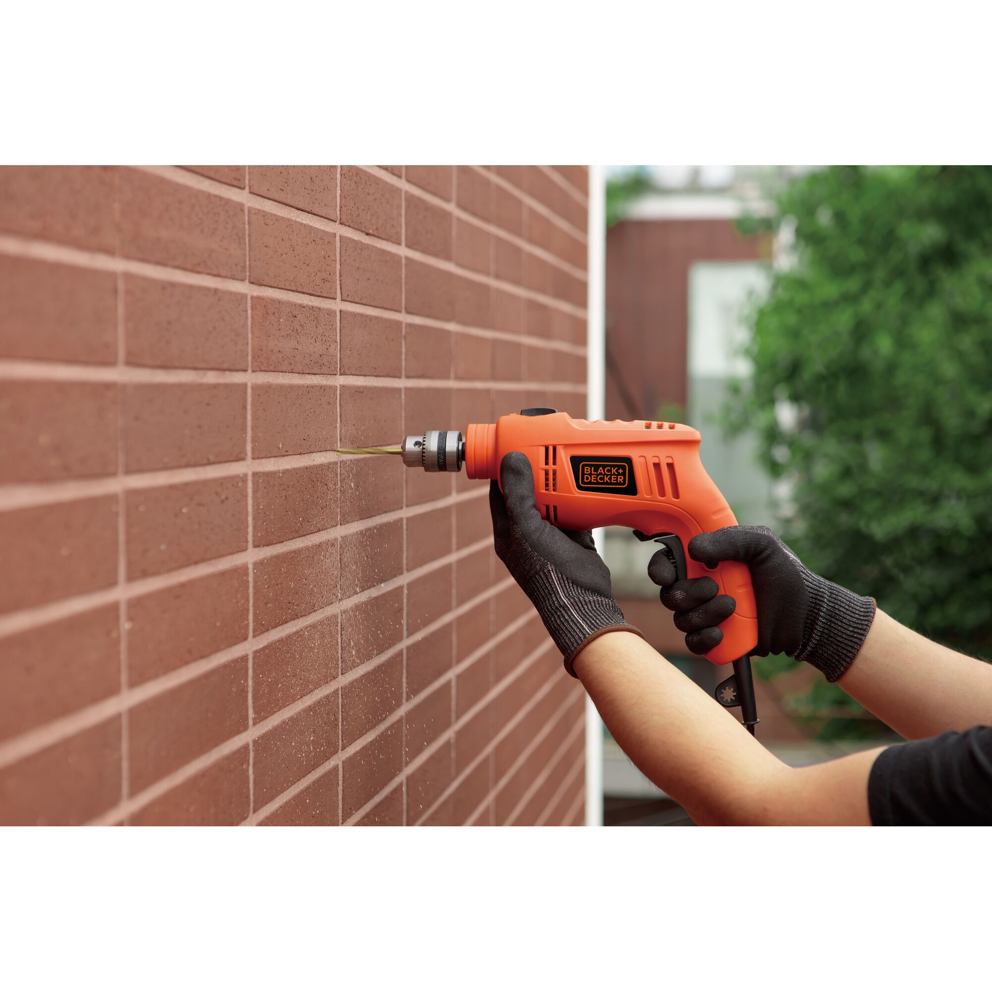 Photography of BLACKDECKER TB555 orange drill in use on red brick wall.