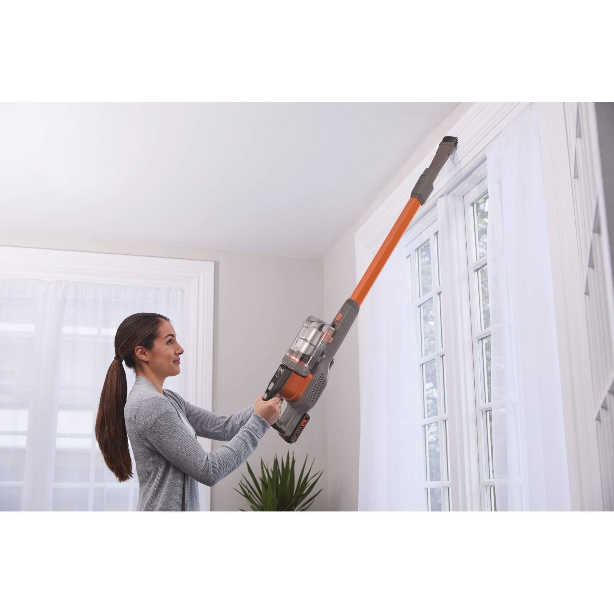 BLACKDECKER TBSV2020S stick vacuum with orange extension tube cleaning high window curtains indoors.