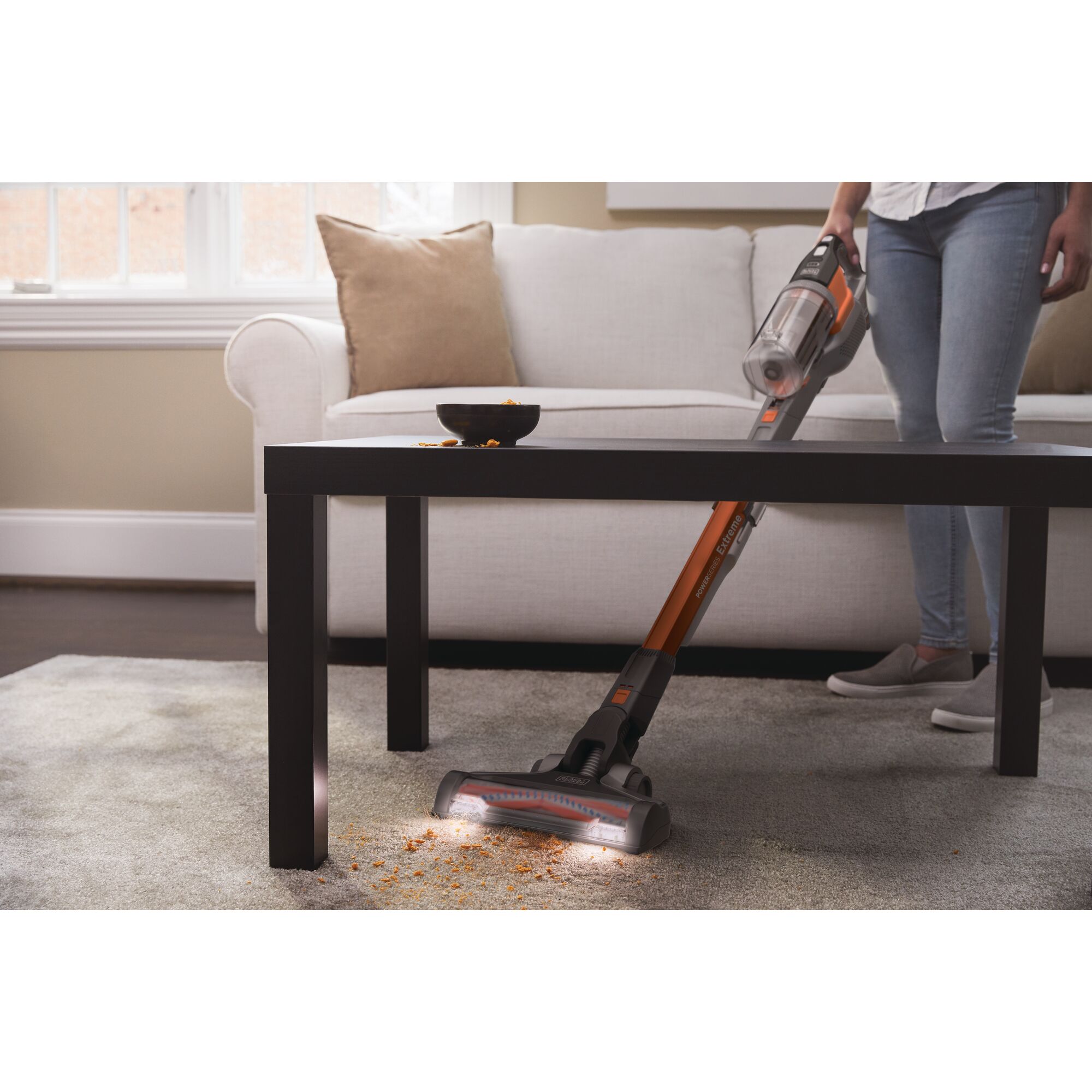 BLACKDECKER TBSV2020S stick vacuum cleaning under coffee table on carpet in living room.