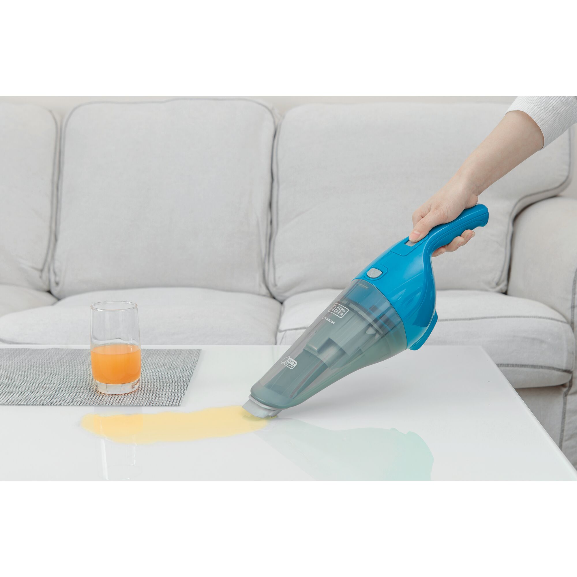 BLACKDECKER WD7201B handheld vacuum cleaning orange liquid spill on white table near glass in living room.