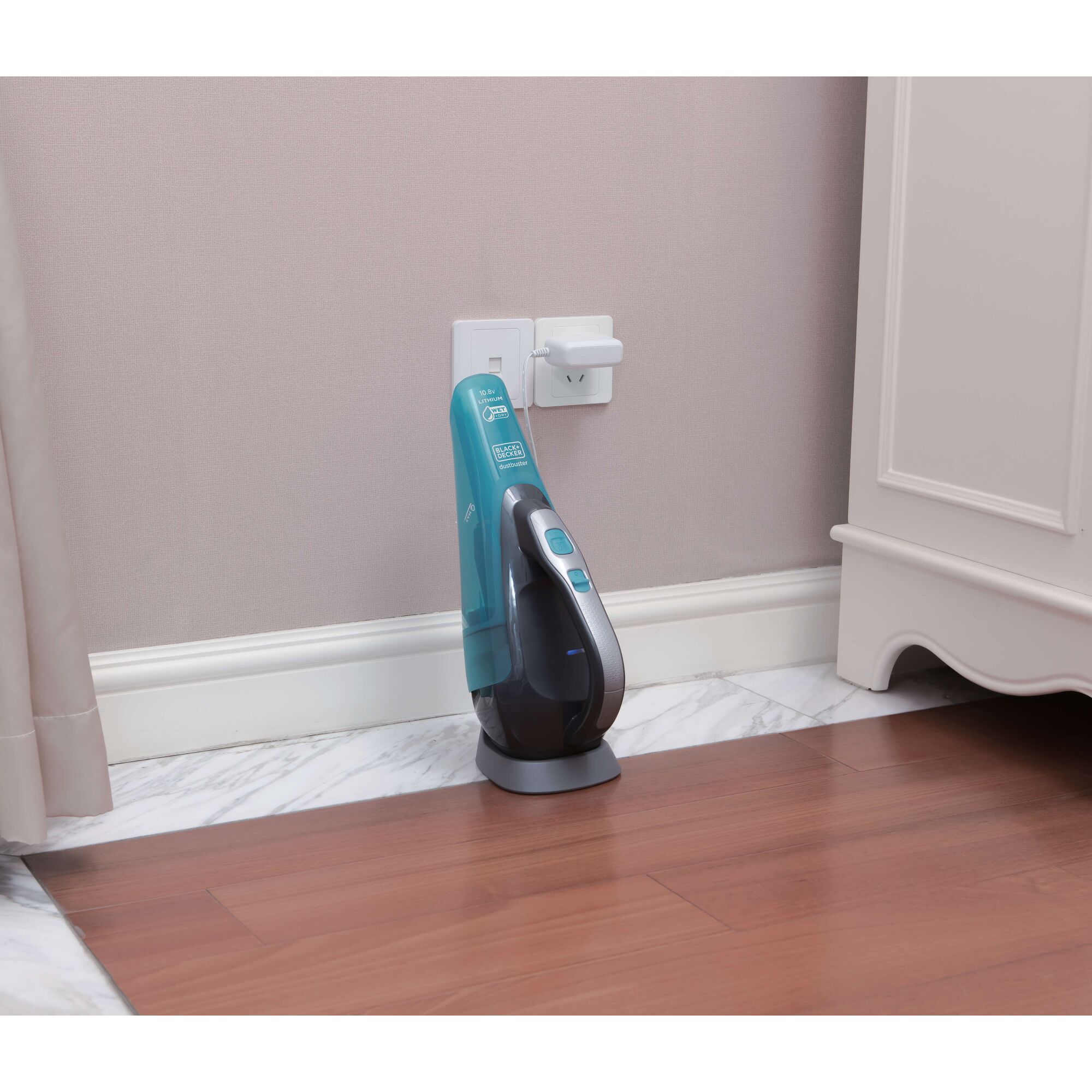 BLACKDECKER WDA320B handheld vacuum in teal, charging upright on docking station against wall on wooden floor.