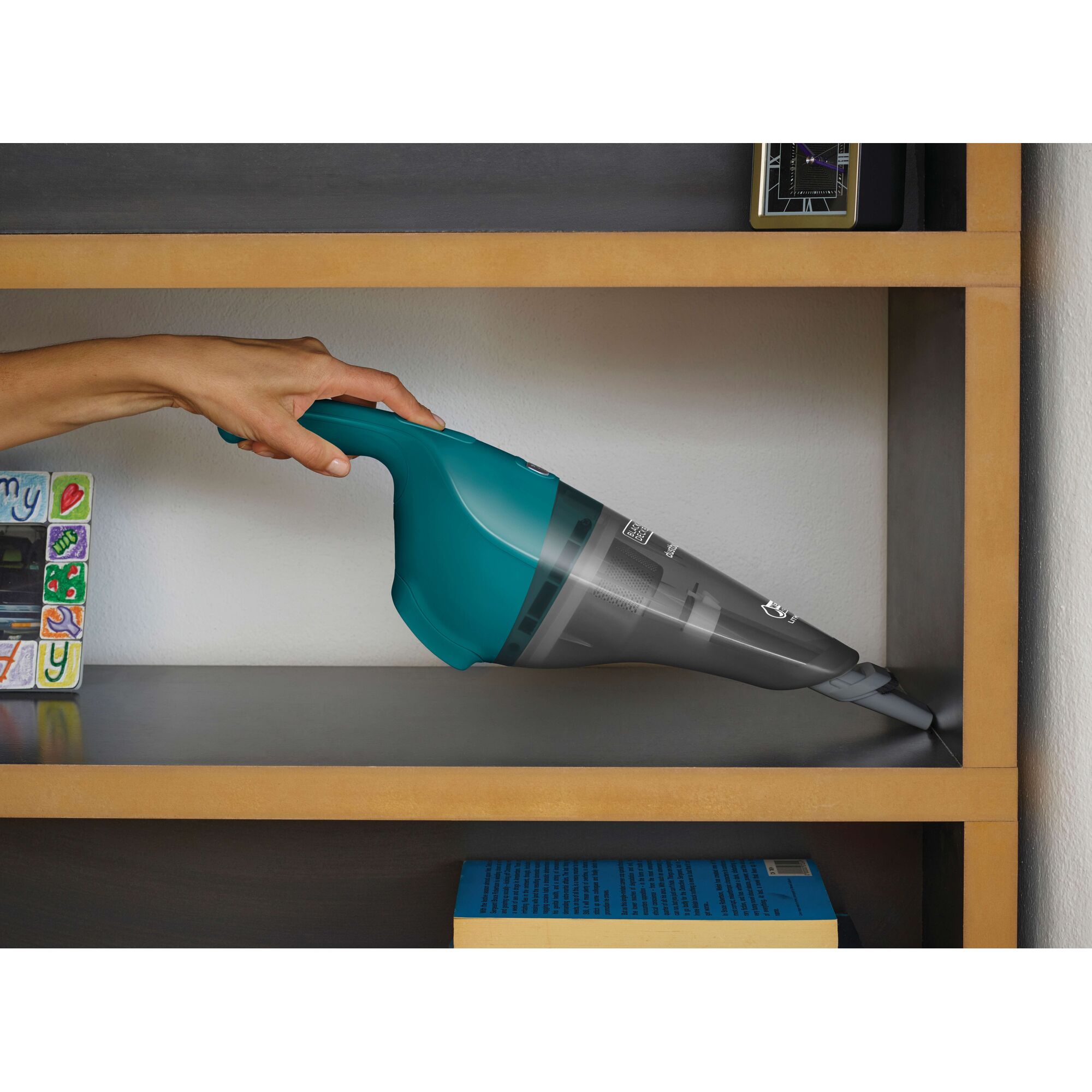A person is using a BLACK+DECKER handheld cordless vacuum cleaner (model WDB115WA) to clean a wooden bookshelf.