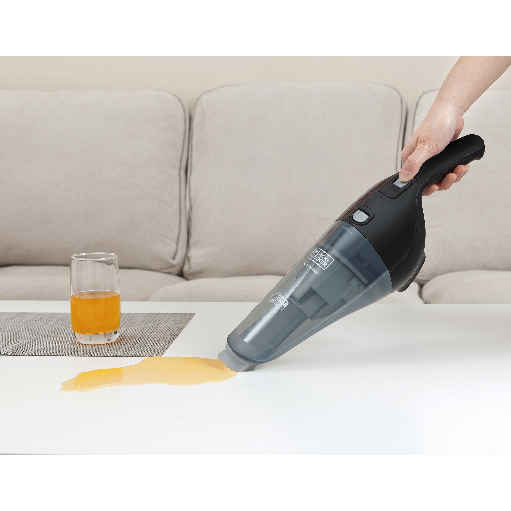 BLACK+DECKER WDB215WBK handheld vacuum cleaning spilled orange liquid from white table near glass, living room setting.