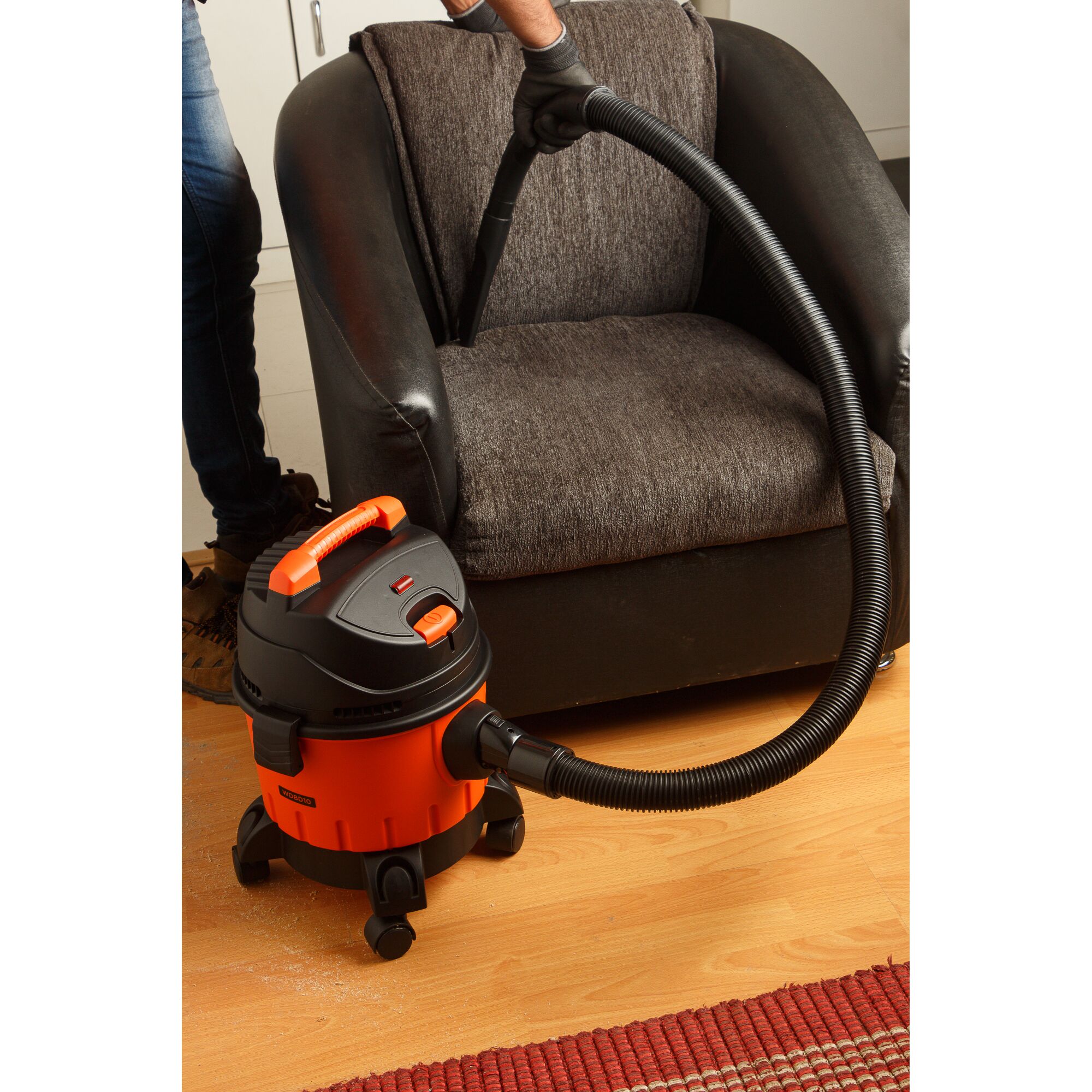 BLACKDECKER WDBD10 orange and black vacuum cleaner cleaning armchair on hardwood floor.