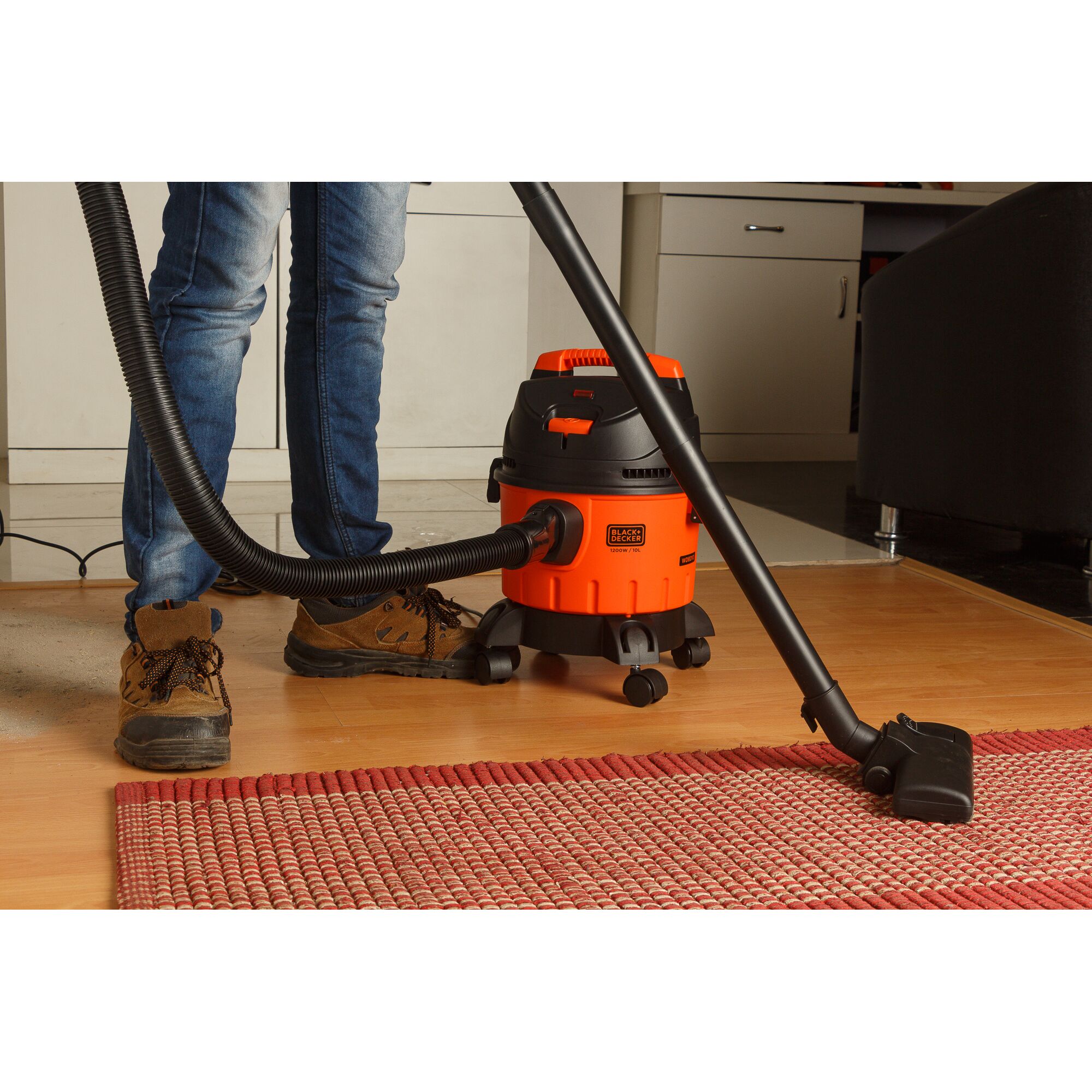 BLACK+DECKER WDBD10 wet and dry vacuum cleaner on wheels cleaning a red rug in a home setting.