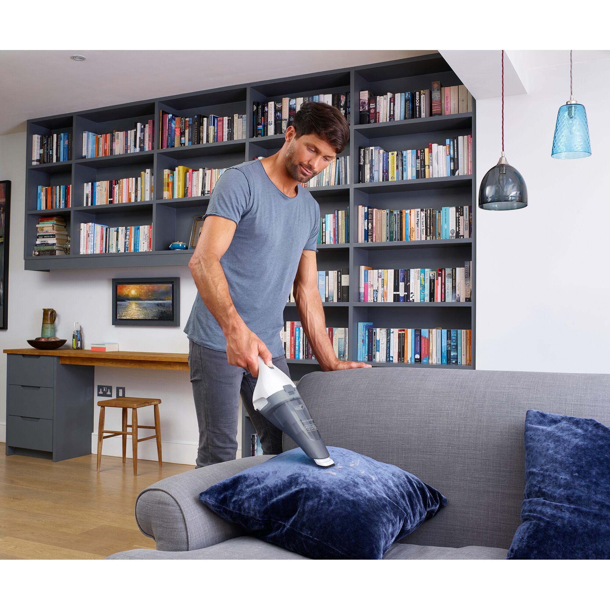 BLACK+DECKER handheld vacuum WDC115W cleaning a blue pillow on a gray sofa in a living room.