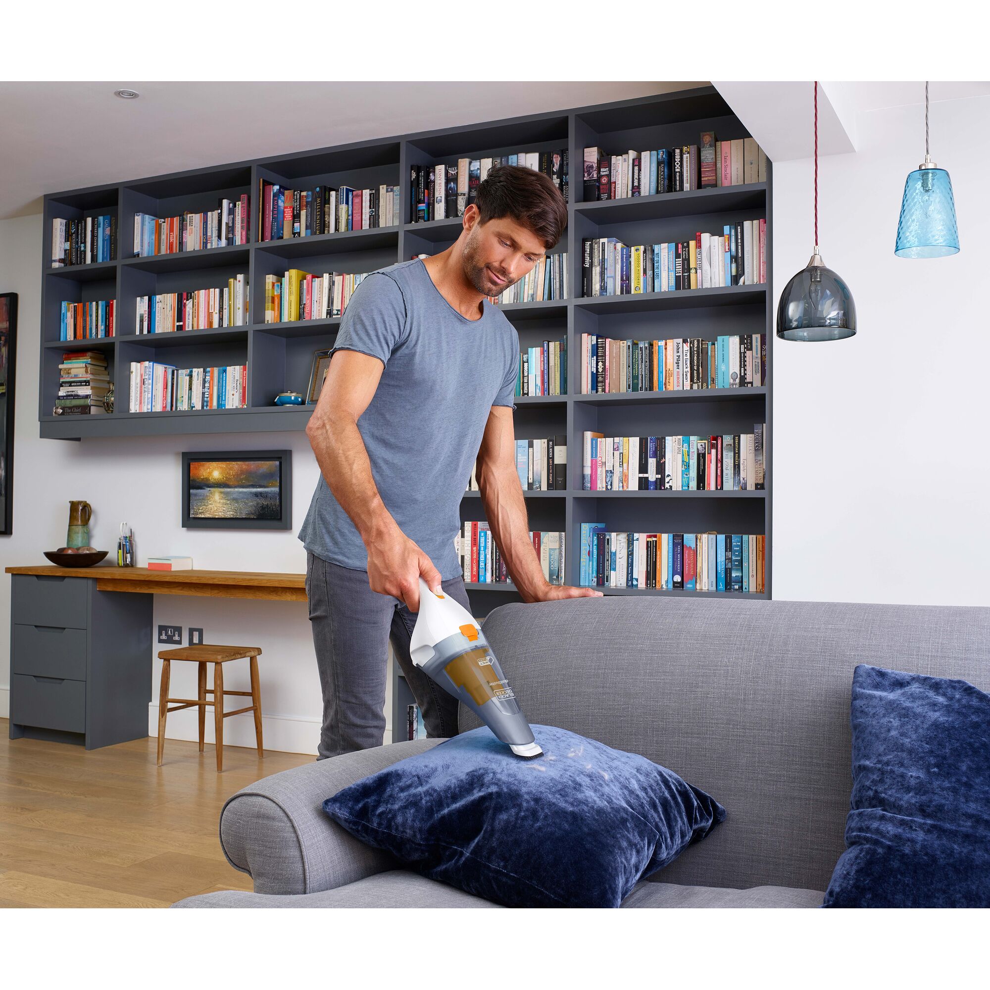 BLACKDECKER WDC215O handheld vacuum cleaning blue pillow on gray sofa in modern living room.